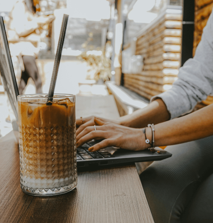 Person typing on a laptop with an ice latte in the foreground