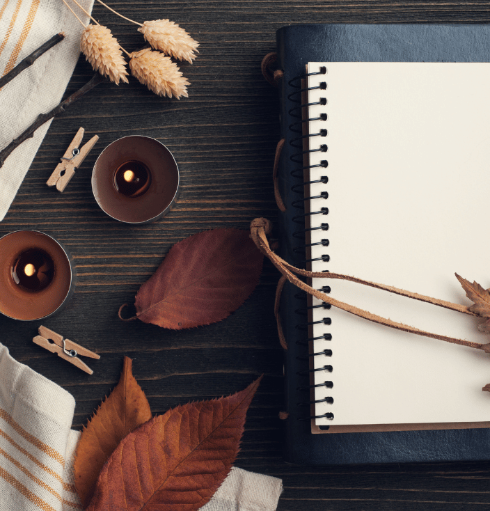 A journal, leaves, and candles sitting on a table